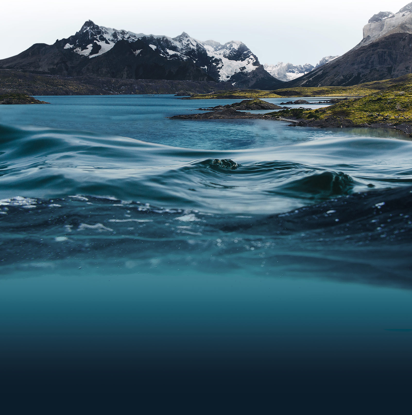 A close up image of the surface of water, with mountains in the background